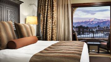 Habitación de hotel con una cama grande, vistas a montañas y un balcón con mesa y sillas.