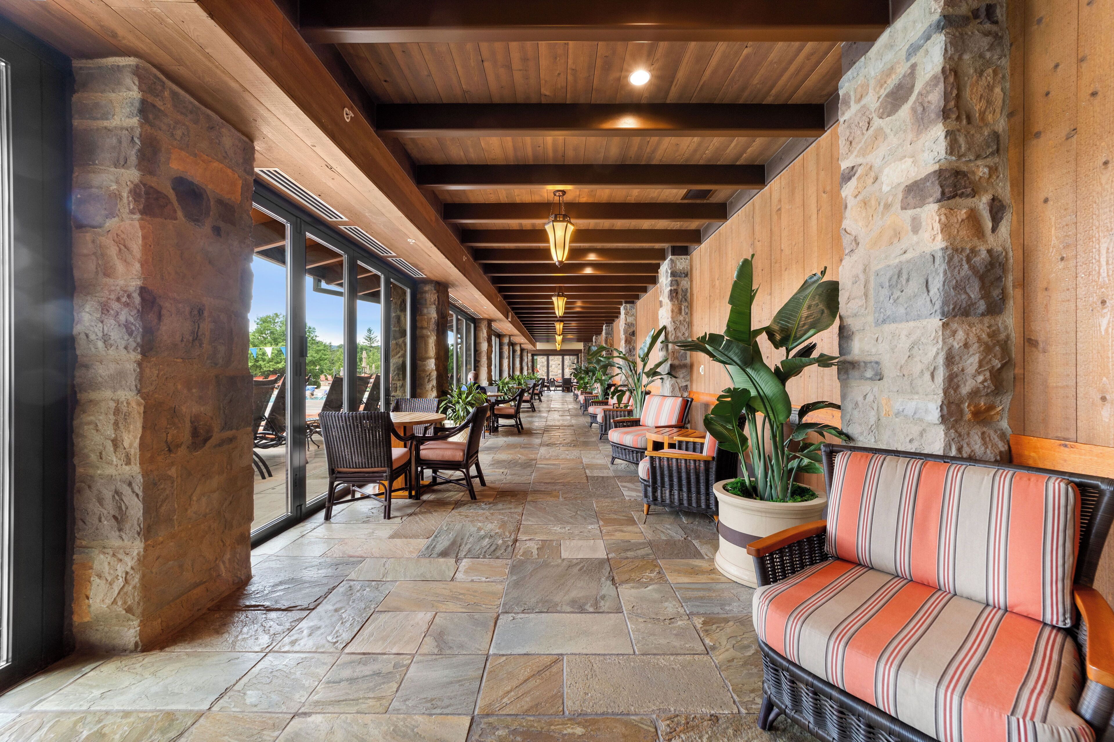 A covered outdoor seating area with stone walls, wooden beams, and potted plants.