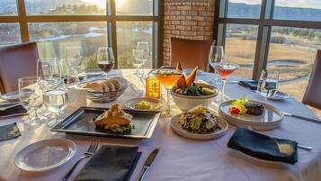 A dining table set with various dishes, glasses, and cutlery, with a view of a landscape through large windows.