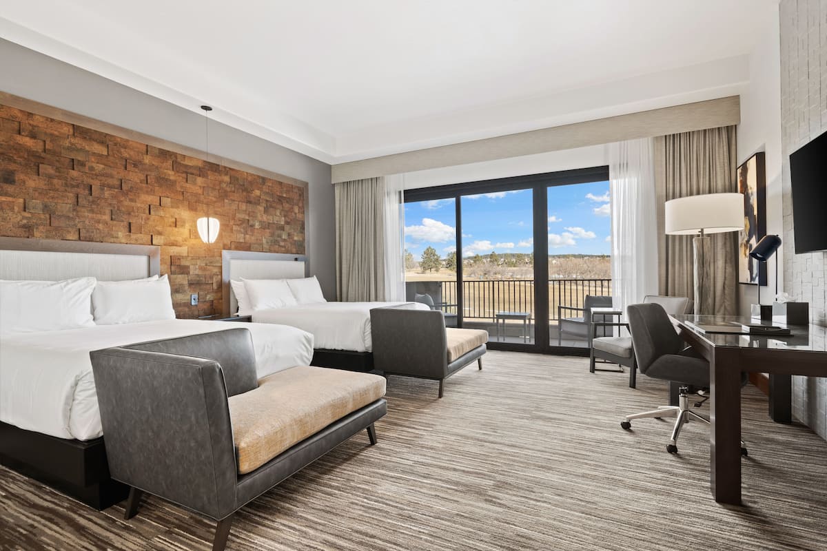 Een hotelkamer met twee bedden, een bureau, een stoel en uitzicht op de omgeving.