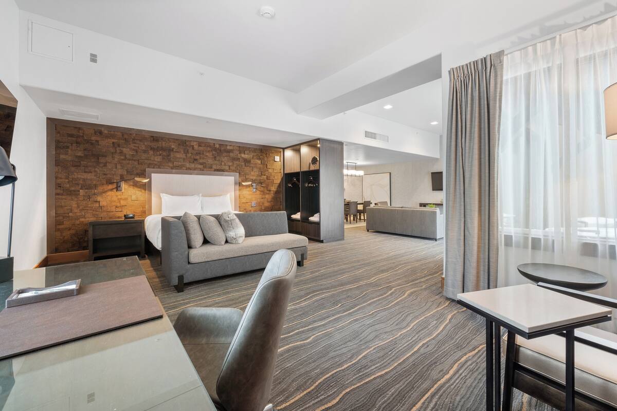 Een moderne hotelkamer met een bank, een glazen salontafel, een klein tafeltje en een zithoek met een divan en stoelen.