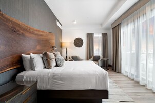 Una habitación de hotel moderna con una cama grande, cabecera de madera, un adorno circular en la pared, un escritorio con silla y ventanas amplias con cortinas.
