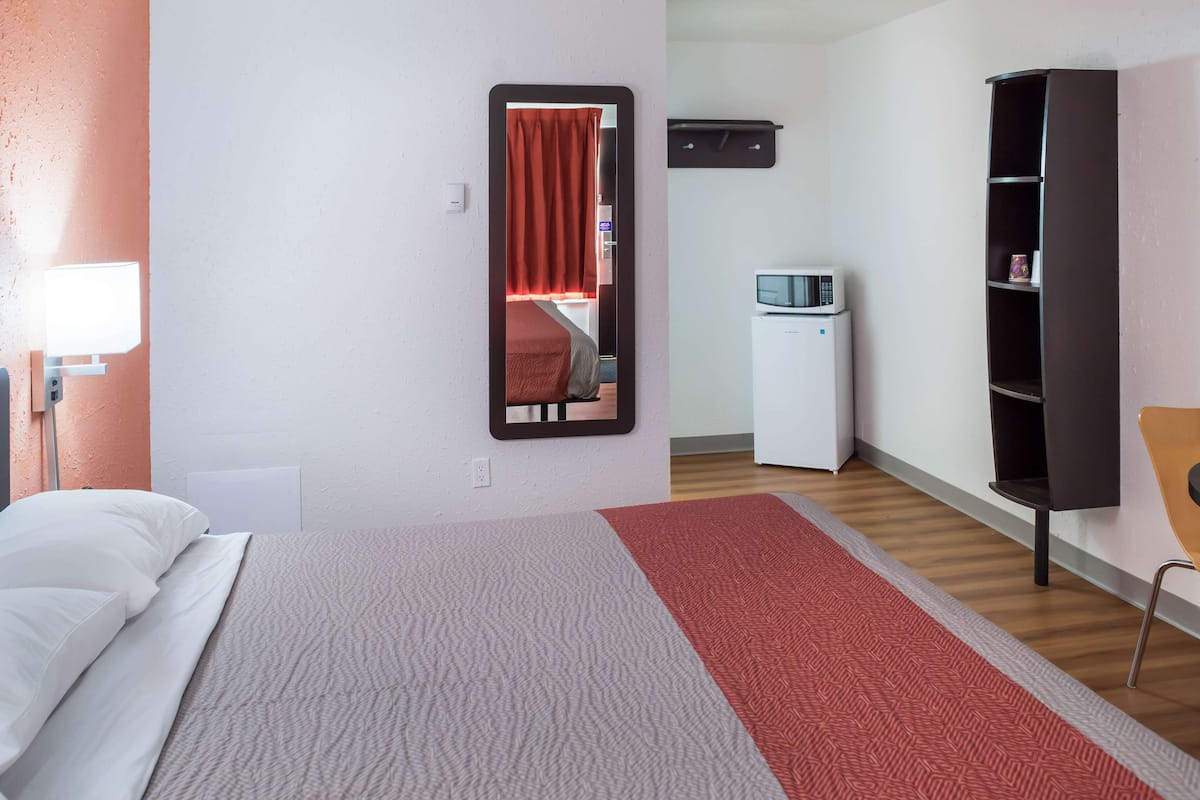 Una habitación de hotel con cama, espejo, televisor, armario y escritorio.