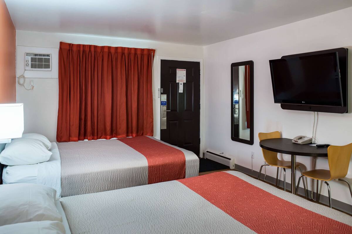 Habitación de hotel con dos camas, televisor, escritorio y sillas, y un espejo.