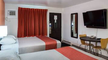 A hotel room with two beds, a TV, a desk with chairs, and a mirror.