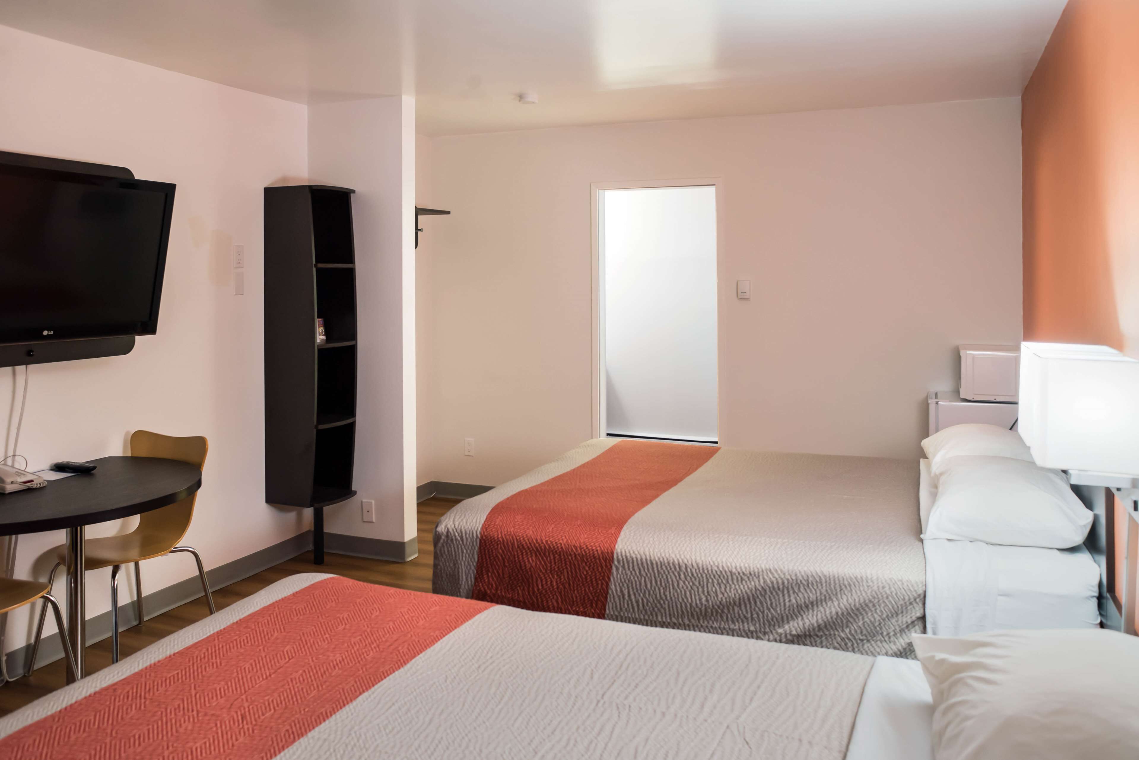 A hotel room with two beds, a TV, a small table with chairs, and a wardrobe.