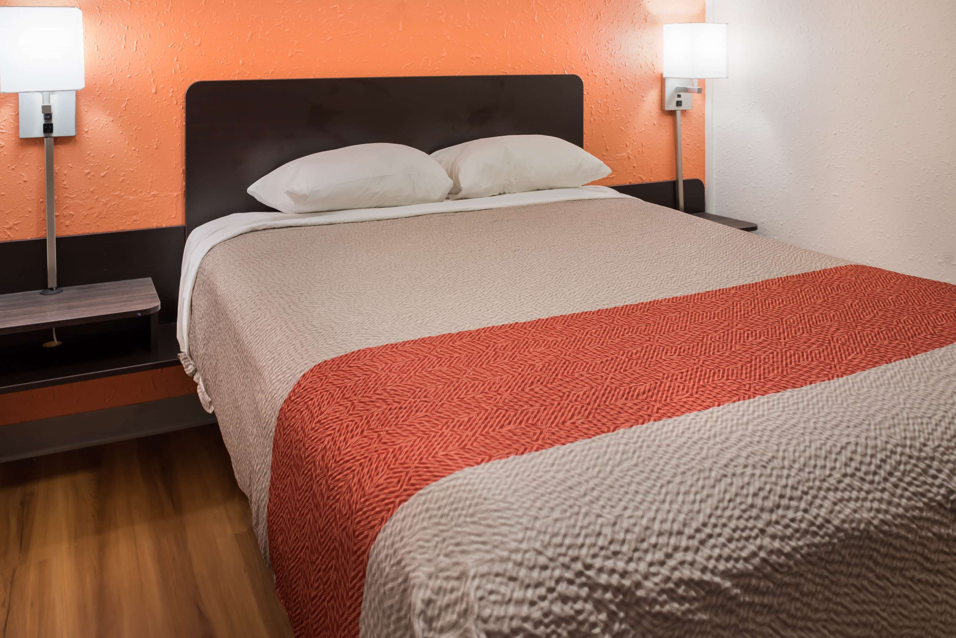 Una cama bien hecha con una colcha blanca y roja, dos lámparas de noche y una mesita de madera.