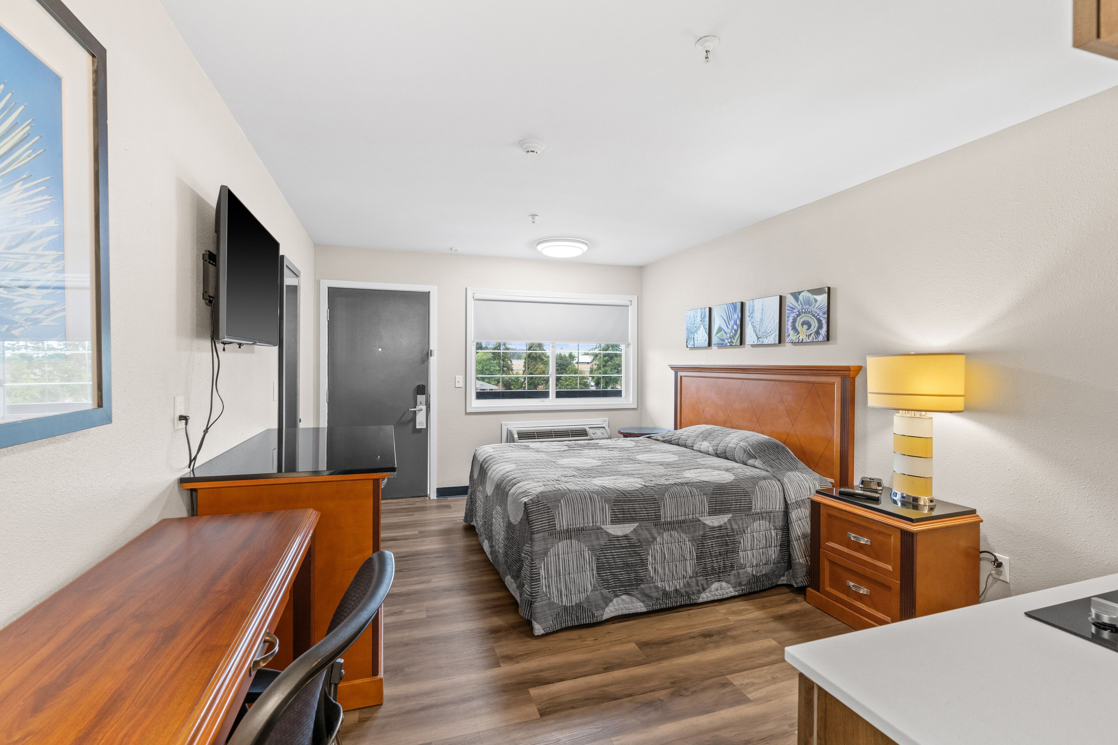 A hotel room with a bed, desk, chair, and a TV mounted on the wall.