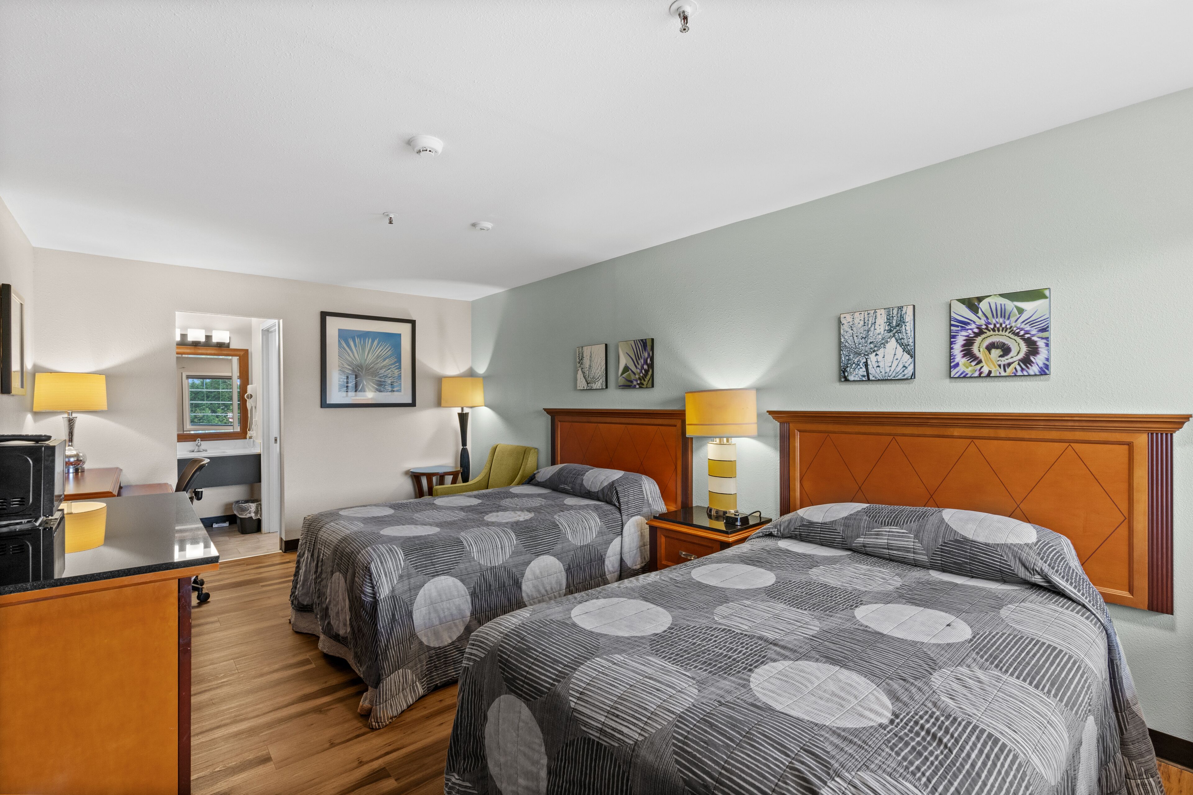 A hotel room with two beds, a desk, a chair, a TV, and artwork on the walls.