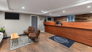 Un área de recepción con un mostrador de madera, sillones de cuero, un tapete estampado y un televisor montado en la pared.