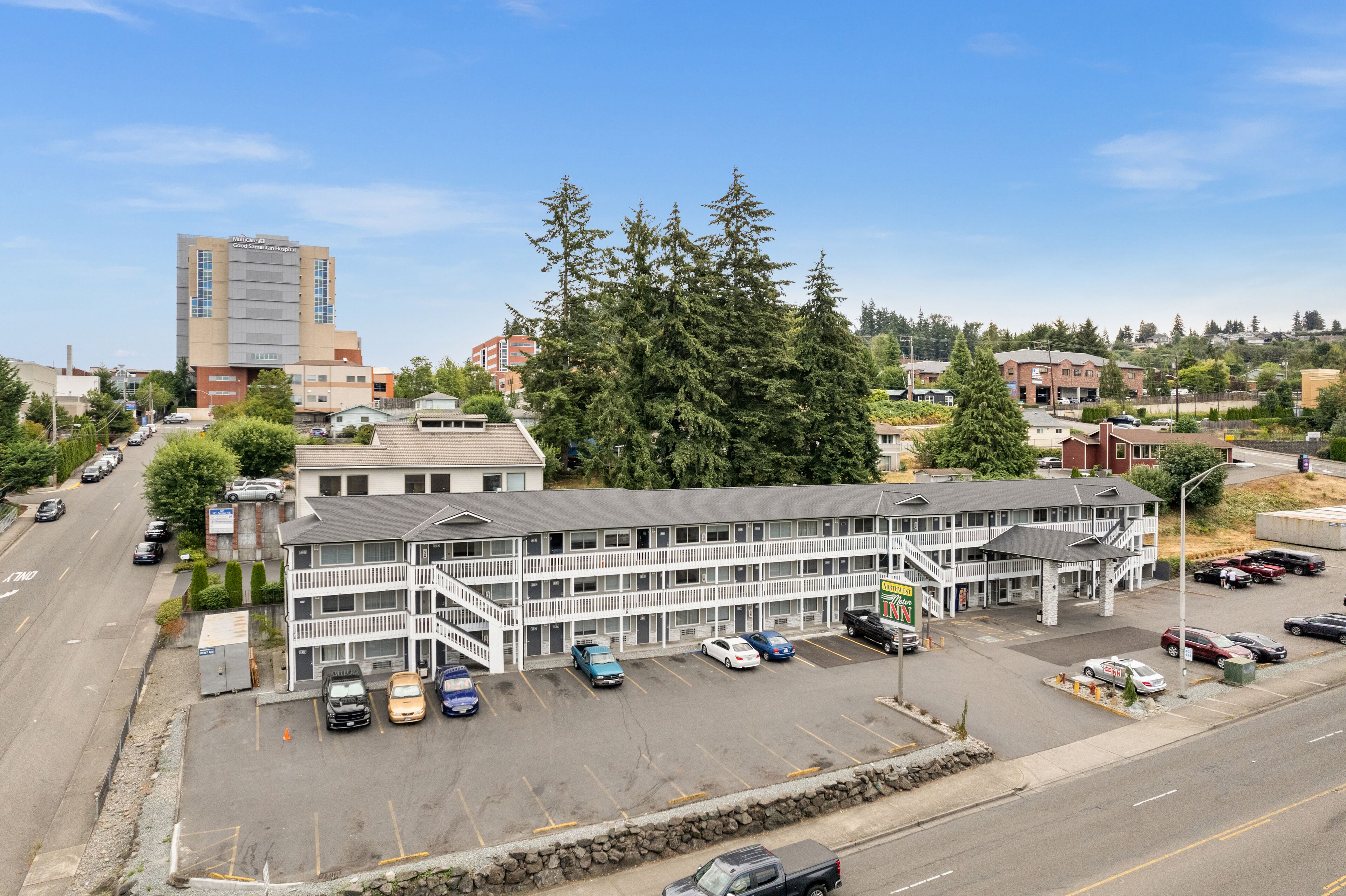 A multi-story motel with a parking lot and a large tree in front.