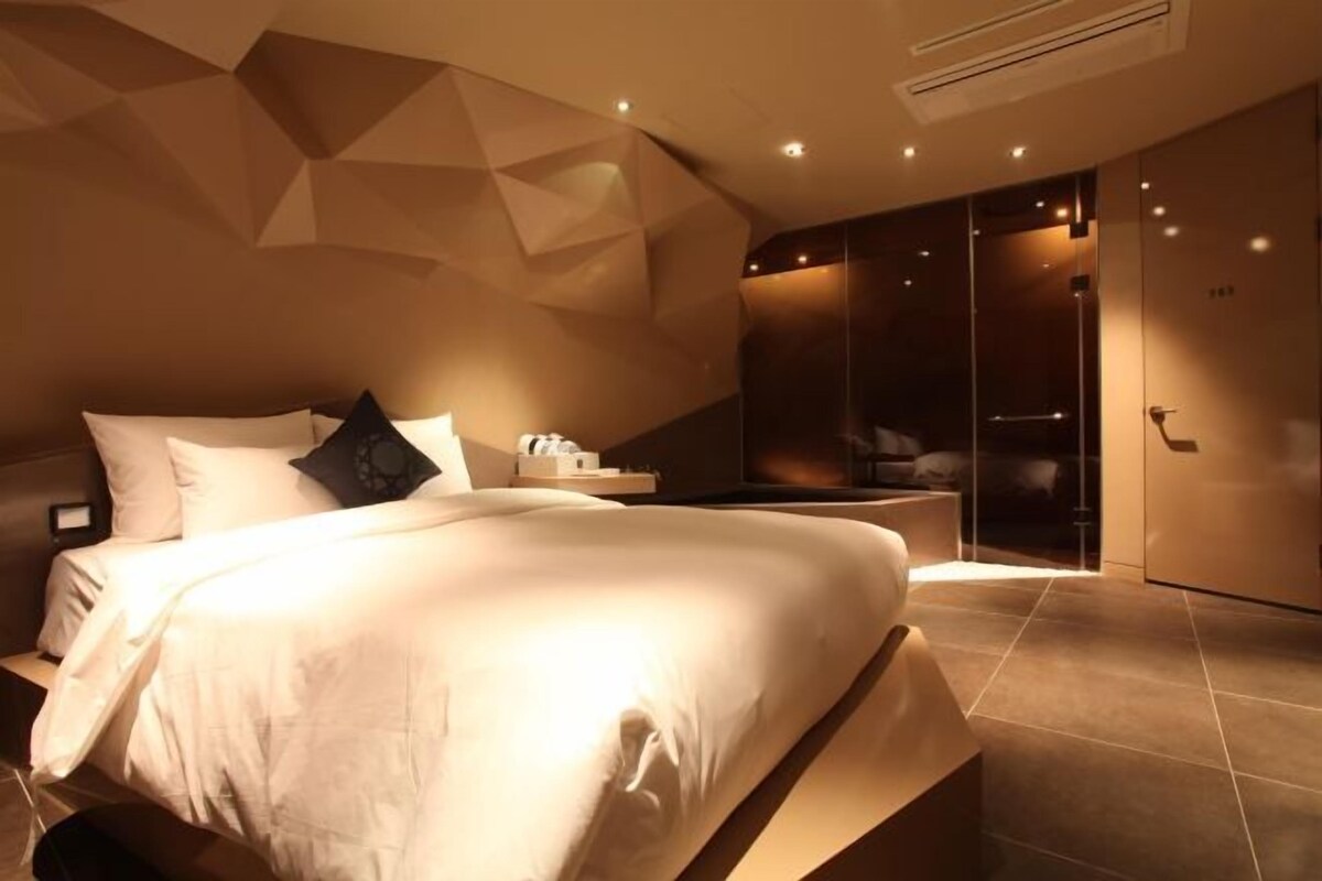 A modern bedroom with a large bed, a nightstand, and a wardrobe.