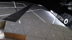 A modern hotel exterior with a geometric tile pattern and a prominent illuminated sign reading "HOTEL CUBAN".