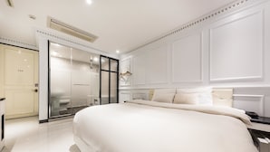 A modern bedroom with a large bed, a walk-in closet, and a glass shower enclosure.