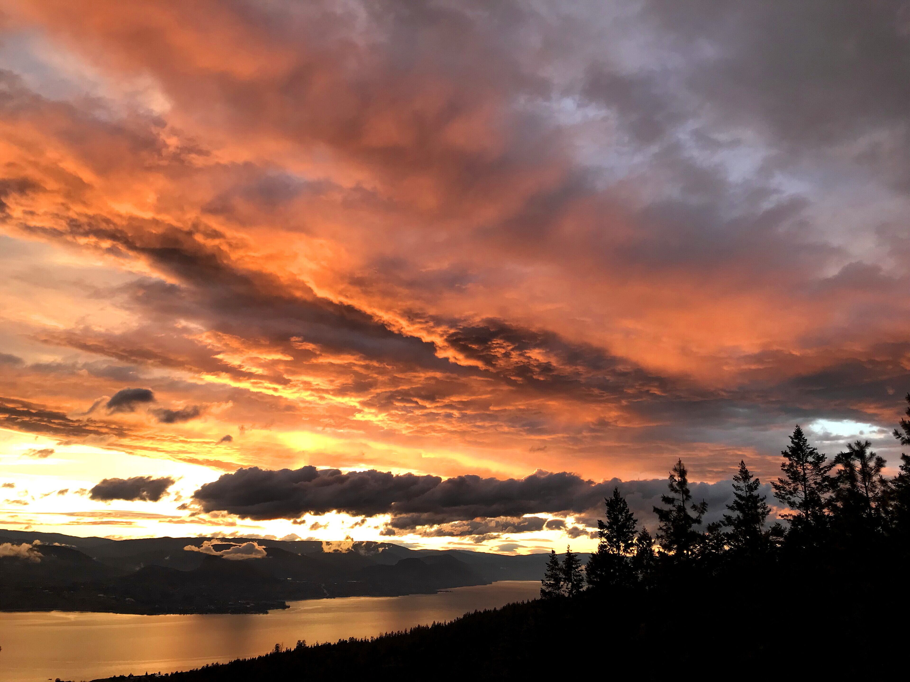 A sunset over a lake with mountains in the background and trees in the foreground.