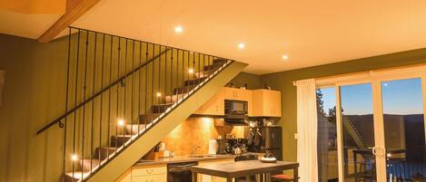 A spacious living area with a high ceiling, a staircase, a kitchen, and a dining area.