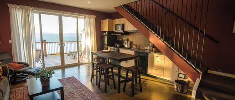 A modern kitchen with a dining area, a staircase, and a large sliding glass door leading to a balcony.