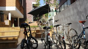 Un patio con bicicletas estacionadas junto a un edificio, un banco de madera y un área de terraza con una mesa y sillas.