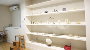 Una habitación con estanterías blancas que exhiben diversos objetos decorativos, un taburete de madera y una mesita con un espejo.