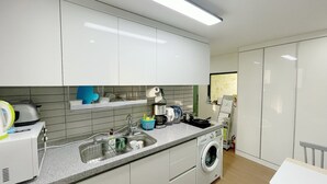 A modern kitchen with white cabinets, a built-in washing machine, and a countertop with various kitchen items. - Dream Comfort (Seoul)