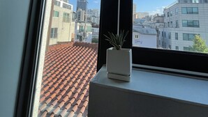 A window with a view of a cityscape, a tiled roof, and a small potted plant on the windowsill. - Dream Comfort (Seoul)