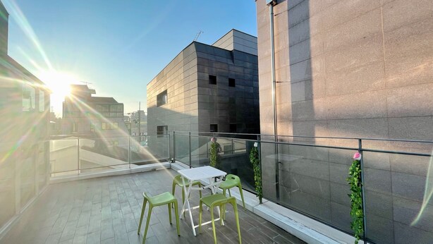 A rooftop terrace with a glass balustrade, green plastic chairs, and potted plants. - Dream Comfort (Seoul)