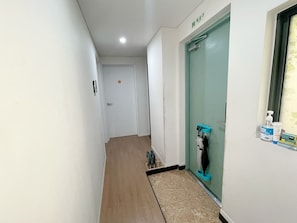 A hallway with a wooden floor, a door with a green sign, and a window with a hand sanitizer dispenser.