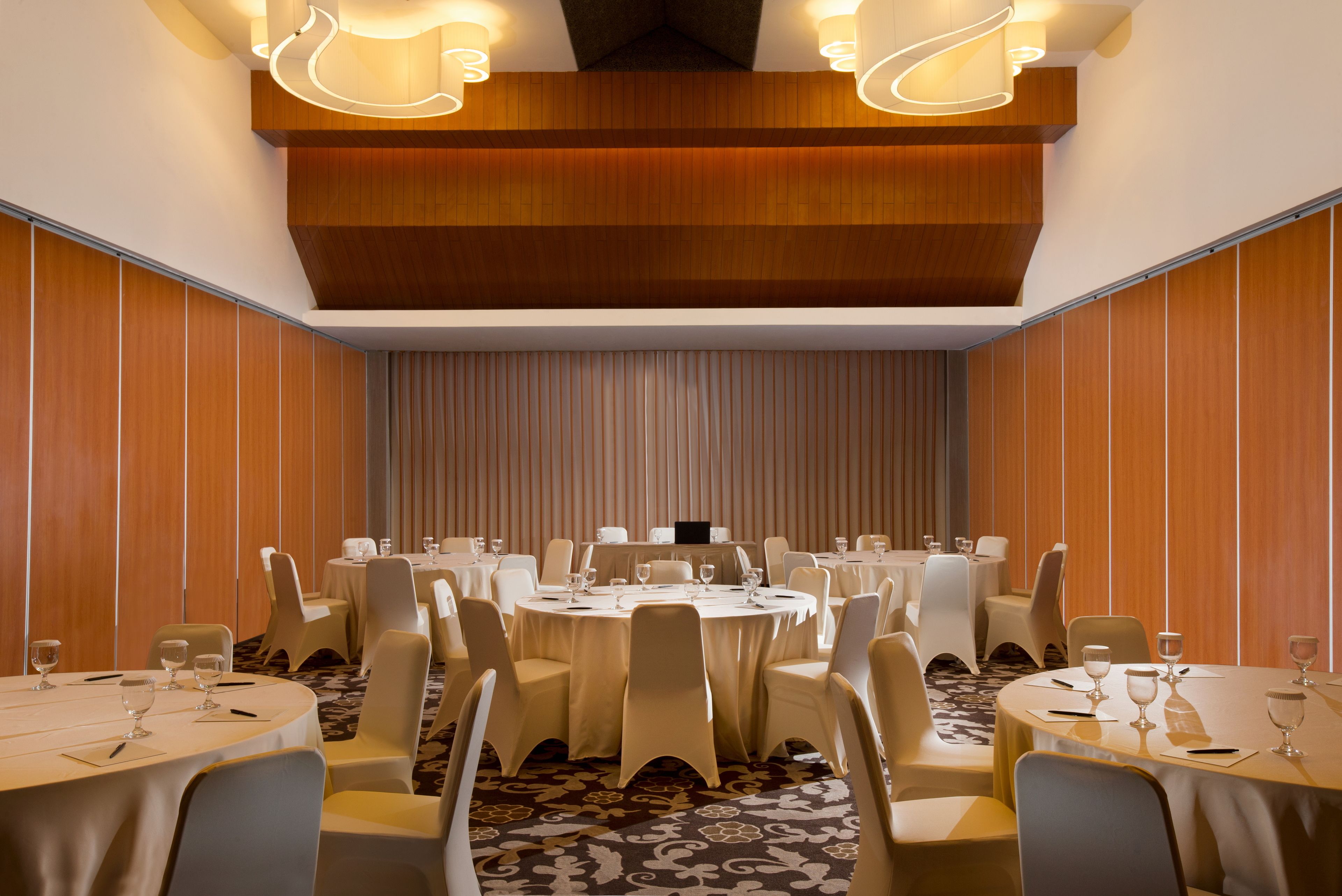 A conference room with round tables, white chairs, and a wooden ceiling.