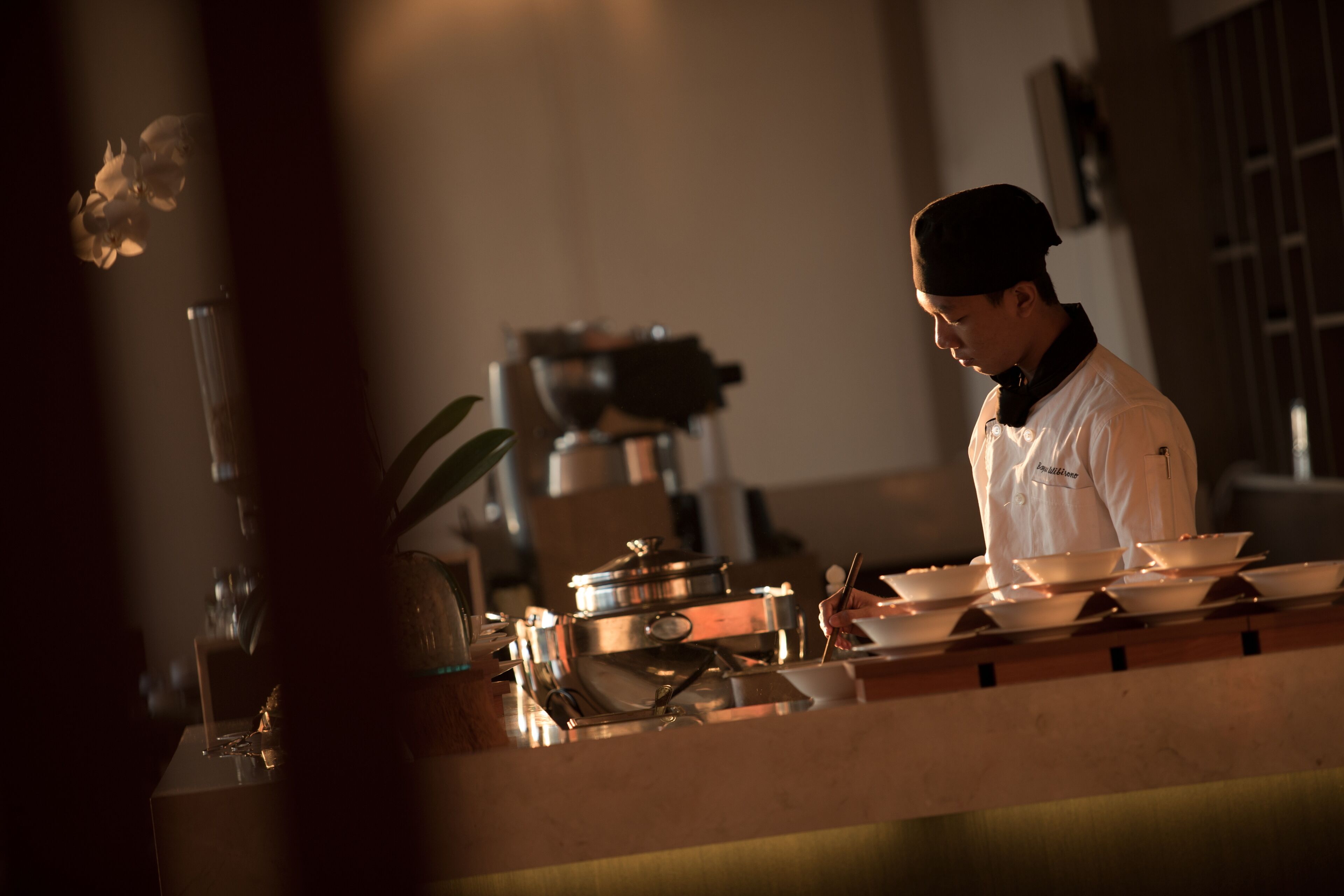 A chef in a white uniform preparing food in a kitchen with stainless steel appliances and a wooden counter.