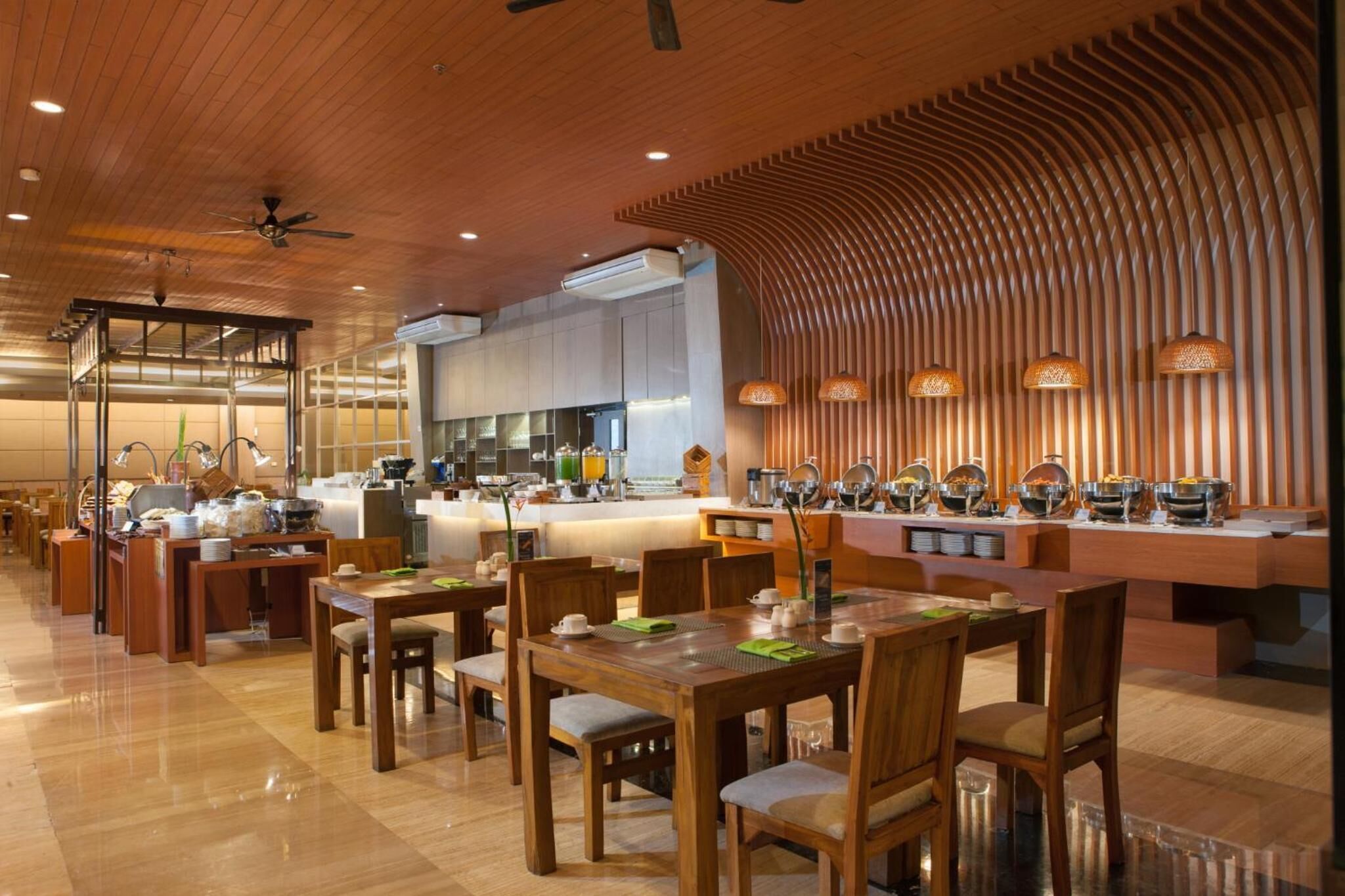 A modern restaurant with wooden furniture, a central counter with food displays, and ambient lighting.