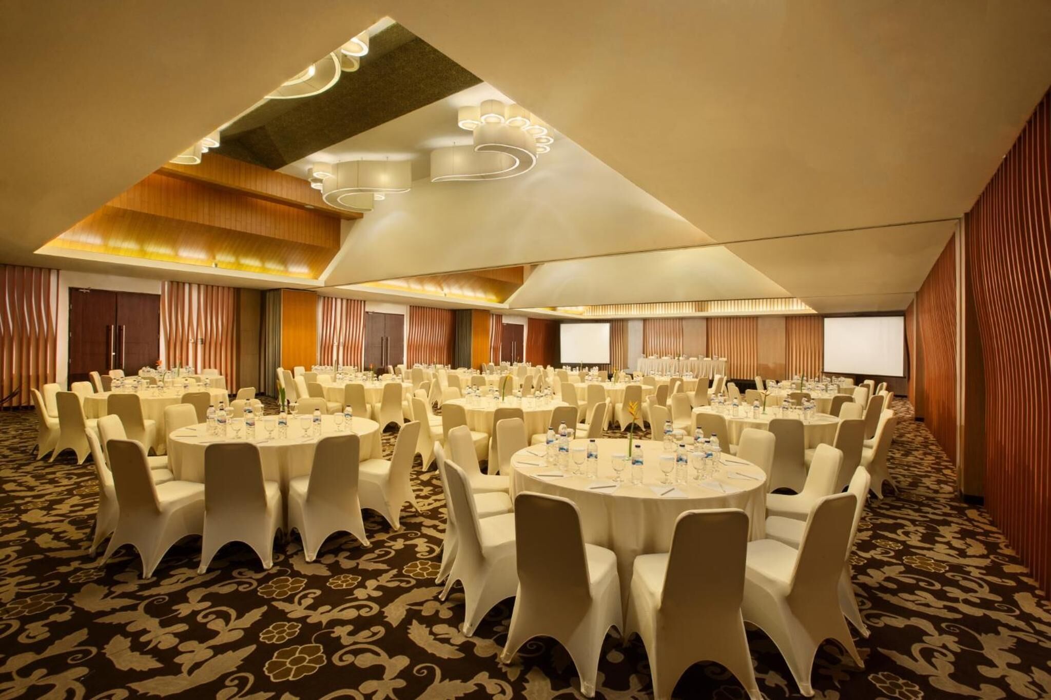 Une salle de banquet avec des tables rondes, des chaises blanches et un sol recouvert de moquette.