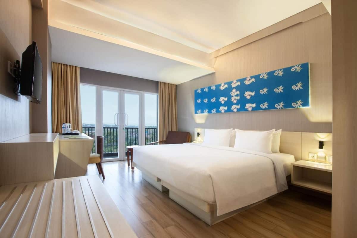 A hotel room with a large bed, a desk, a chair, a TV, and a balcony with curtains.