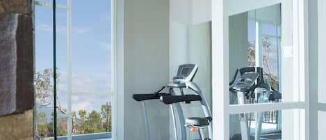 A modern gym with a treadmill and a stationary bike, large windows offering a view of the outdoors.