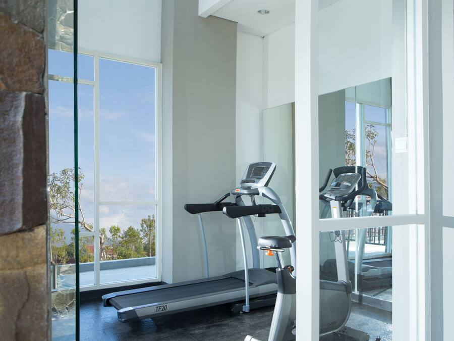 A modern gym with a treadmill and a stationary bike, large windows offering a view of the outdoors.