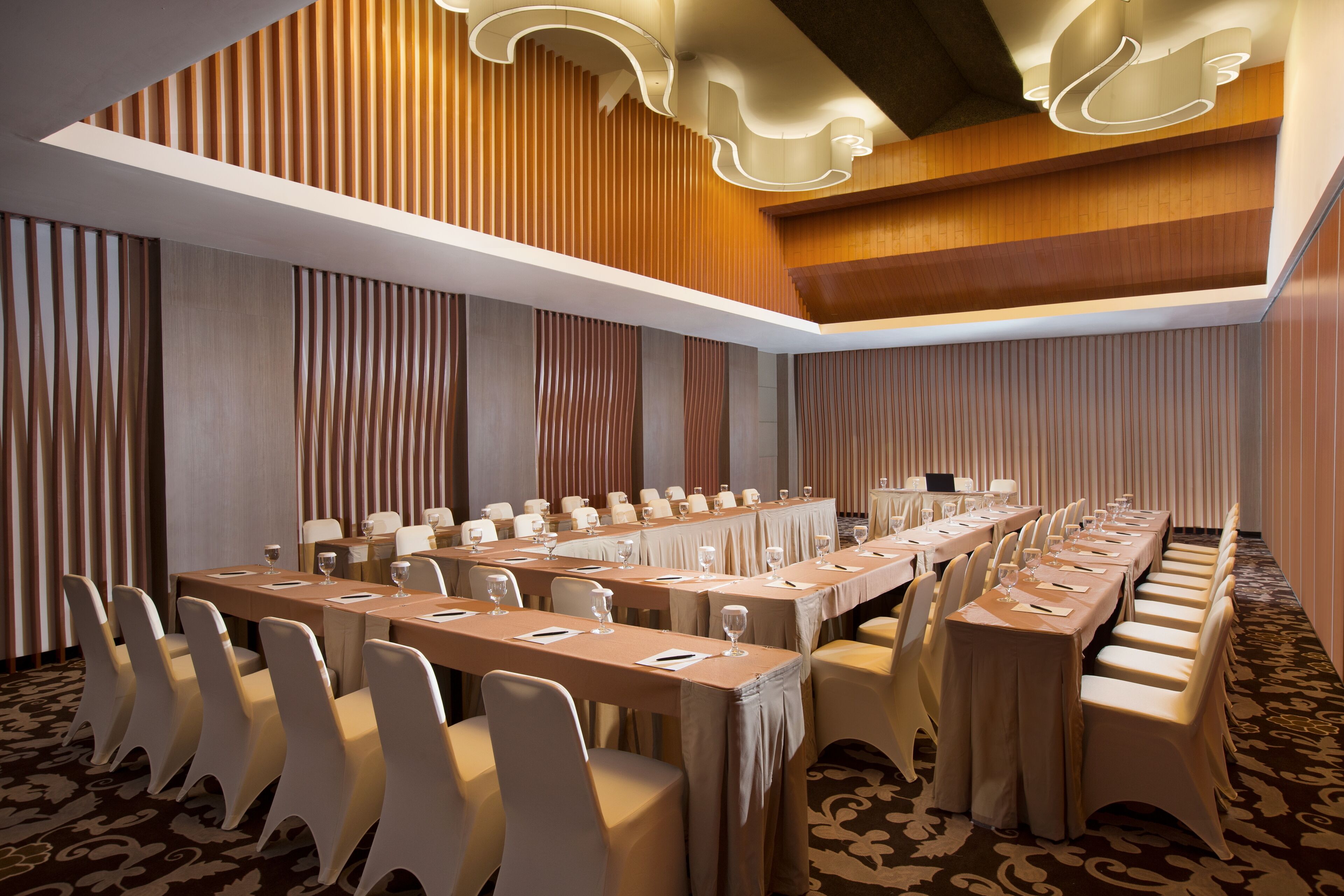A conference room with long tables and chairs, wooden paneling, and a patterned carpet.