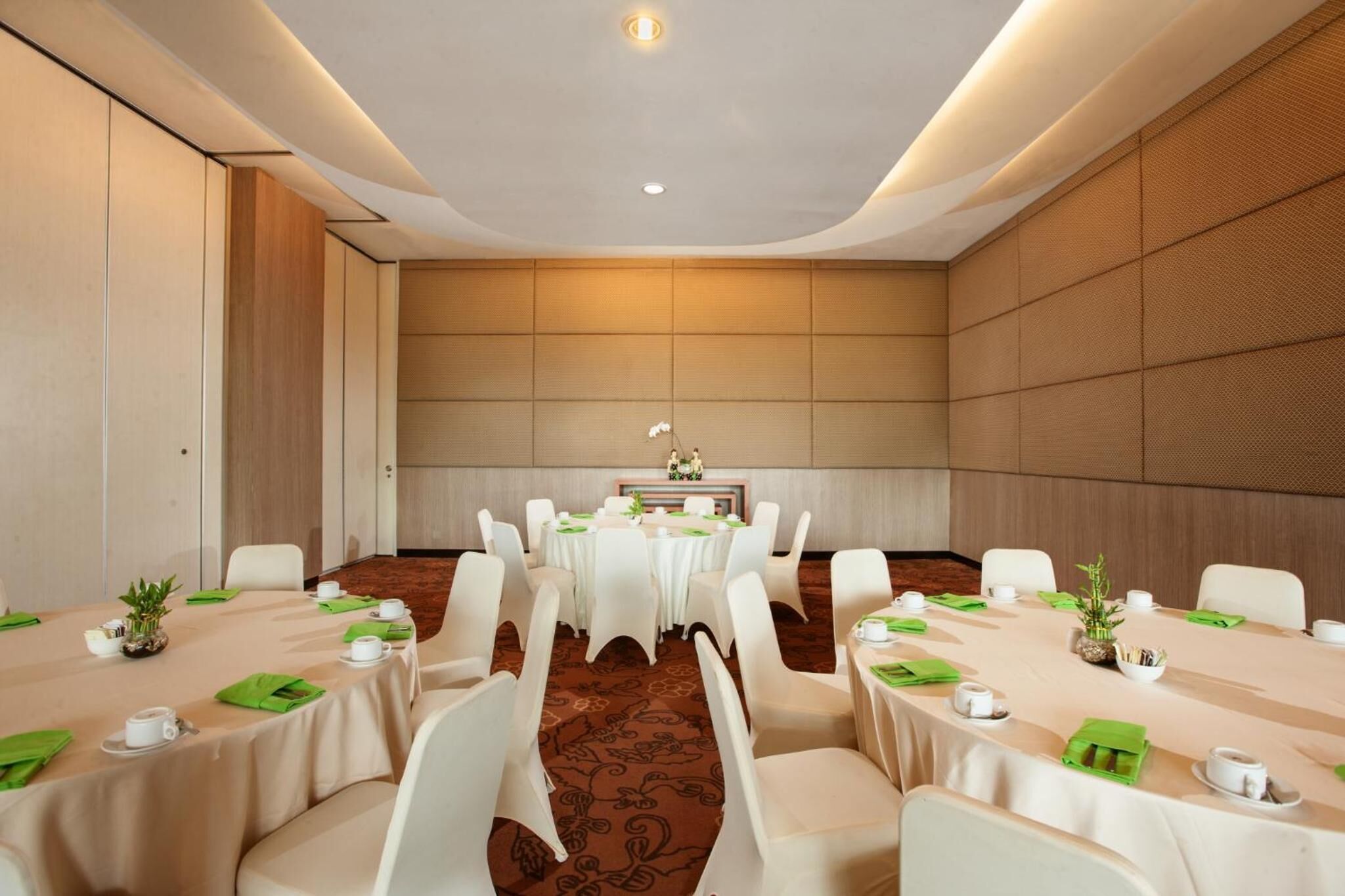 Une salle de conférence avec des tables rondes, des chaises blanches et une table centrale agrémentée d’un arrangement floral.