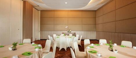 Une salle de conférence avec des tables rondes, des chaises blanches et une table centrale agrémentée d’un arrangement floral.