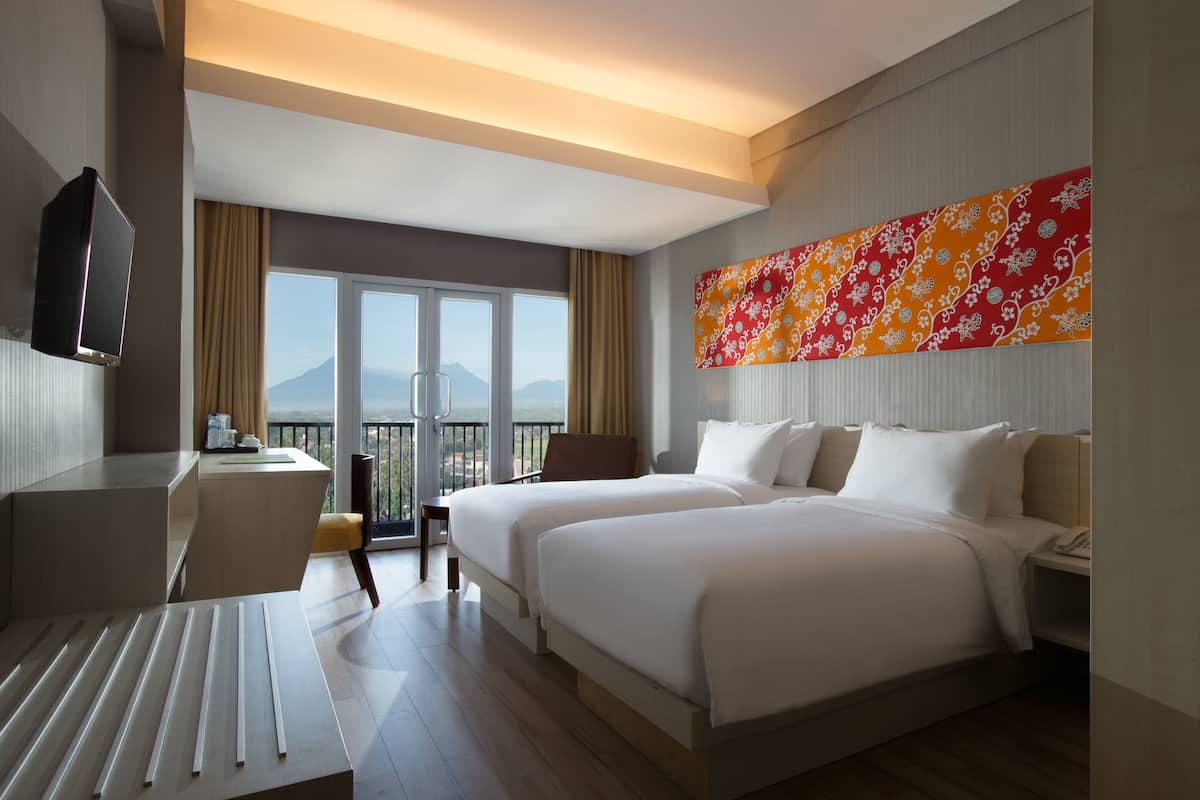 A hotel room with two beds, a desk, a chair, and a TV.