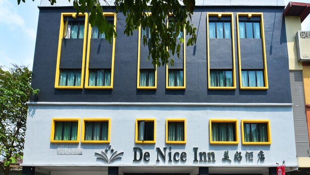 A hotel named De Nice Inn with a modern facade, multiple windows with yellow frames, and a signboard with the hotel name.