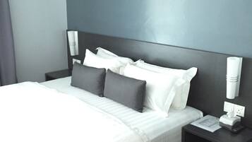 Quarto de hotel moderno com uma cama grande, paredes cinzentas e uma mesa de cabeceira com abajur e telefone.
