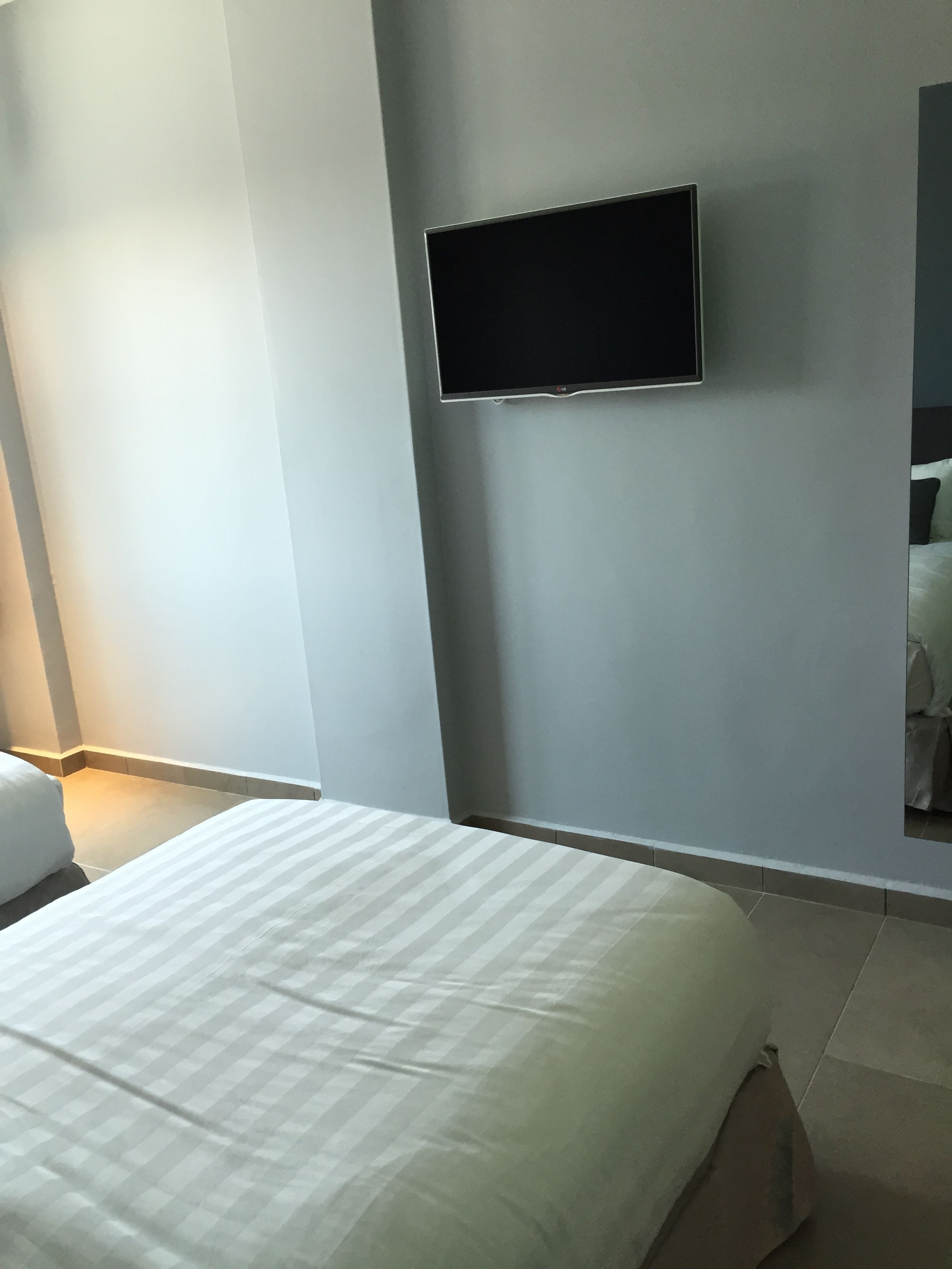 Quarto de hotel com uma cama, uma televisão de tela plana na parede e uma janela pequena.