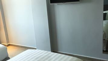 Quarto de hotel com uma cama, uma televisão de tela plana na parede e uma janela pequena.