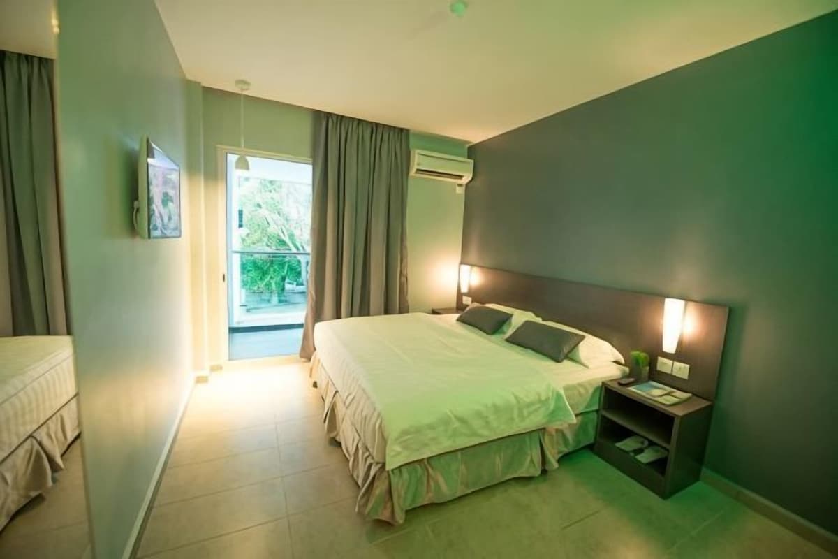 A hotel room with a bed, bedside table, nightstand, and a view of the outdoors.