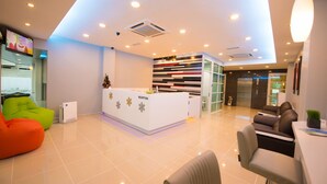 A modern reception area with a white desk, colorful bean bag chairs, and a reception desk with a decorative panel. - G langkawi Motel (Langkawi)