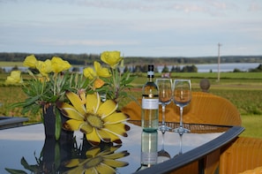 A table with a bottle of wine, two glasses, and a vase of yellow flowers. - Greenwich Moonlight Bay Cottage (Greenwich)