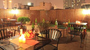 Un patio al aire libre con mesas y sillas, plantas en macetas y una mesa dispuesta con velas.