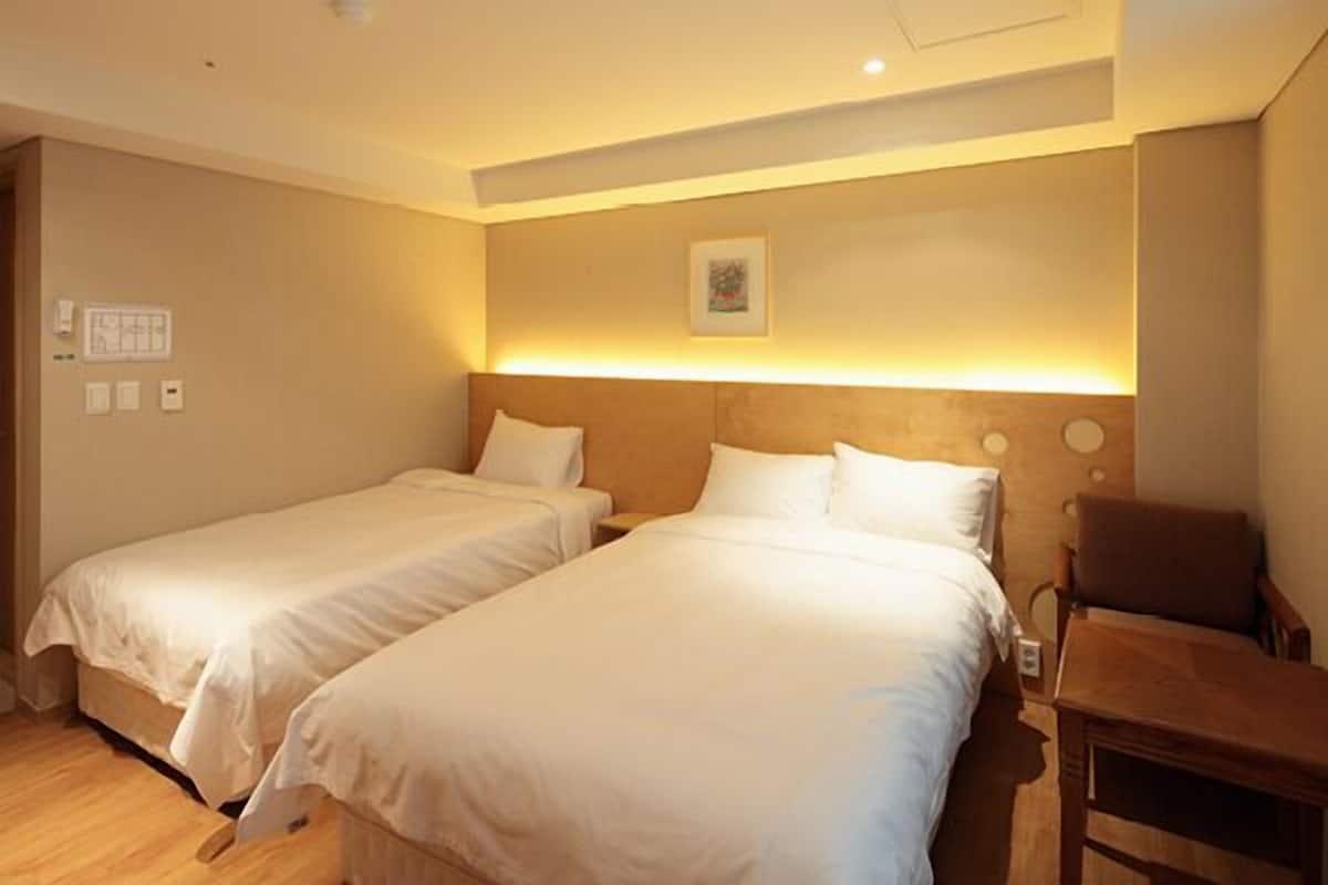A hotel room with two single beds, a wooden nightstand, a chair, and a wall-mounted light fixture.