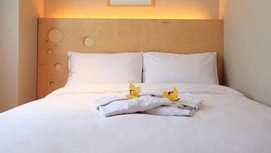 Una cama bien hecha con sábanas blancas y una toalla doblada, junto a dos flores amarillas.