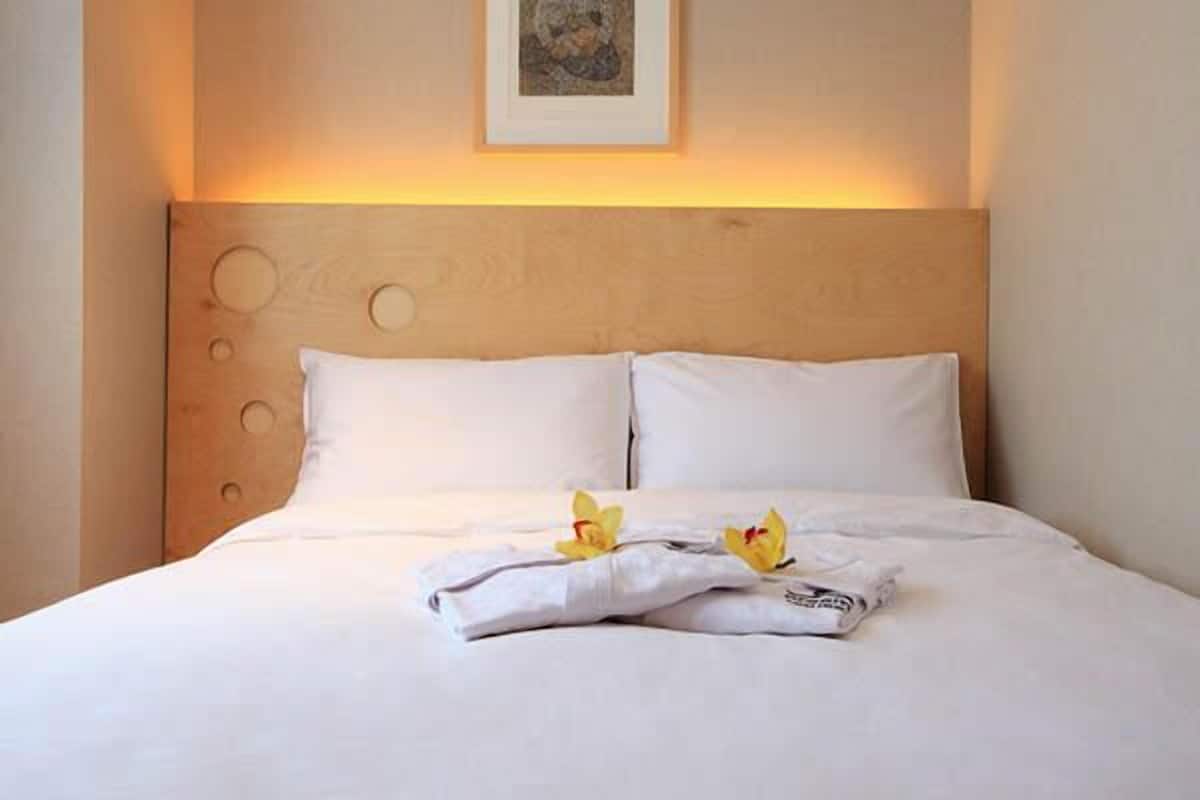 A neatly made bed with white linens and a folded towel, accompanied by two yellow flowers.