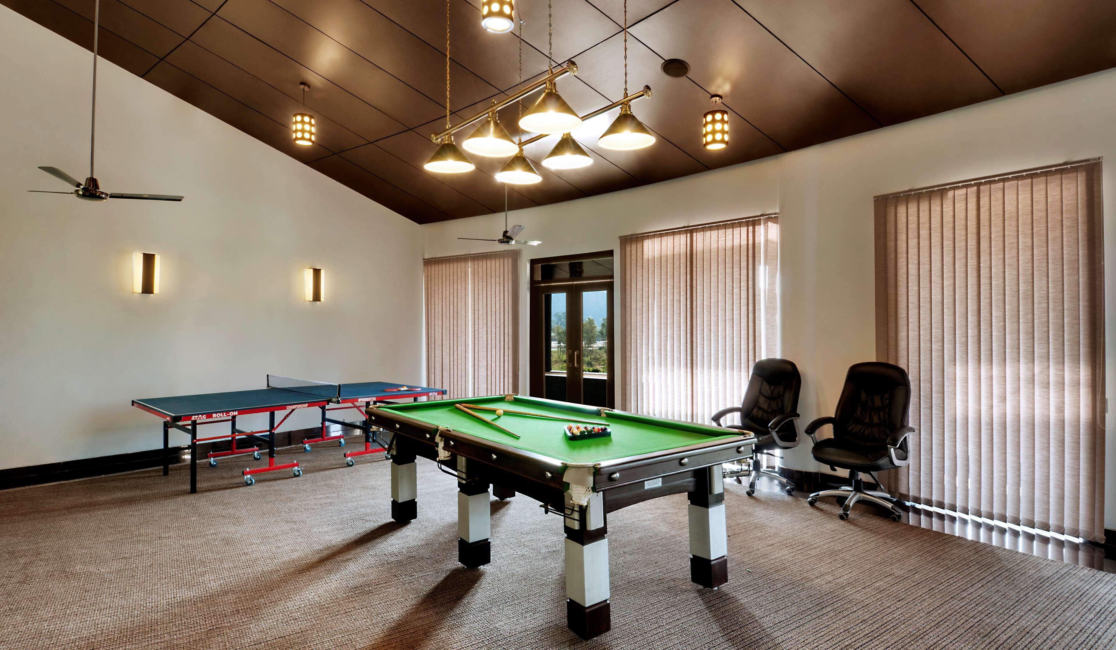 A room with a pool table, two chairs, a ceiling fan, and a window with blinds.